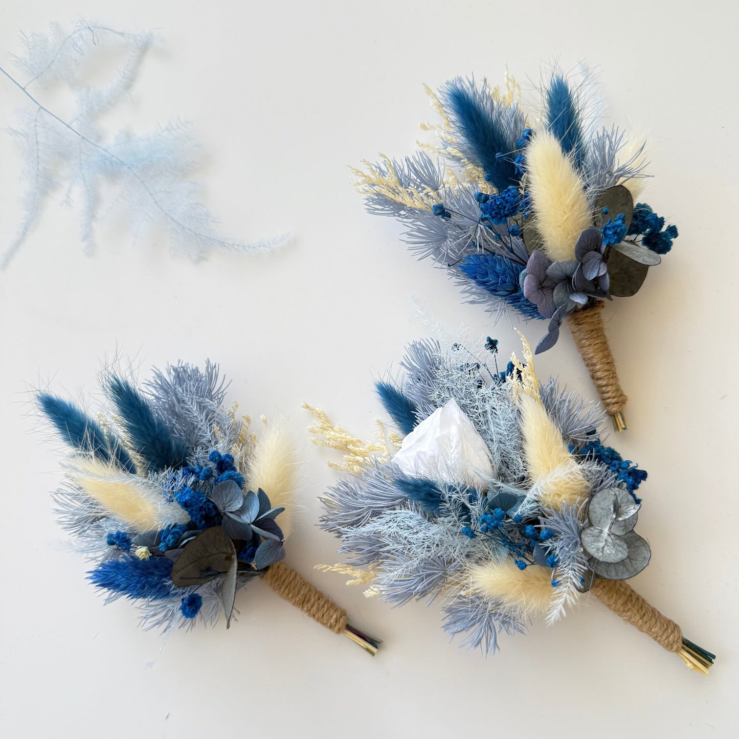 Set of three handmade blue and beige dried boutonnieres with natural jute stems, perfect for groomsmen gifts.
