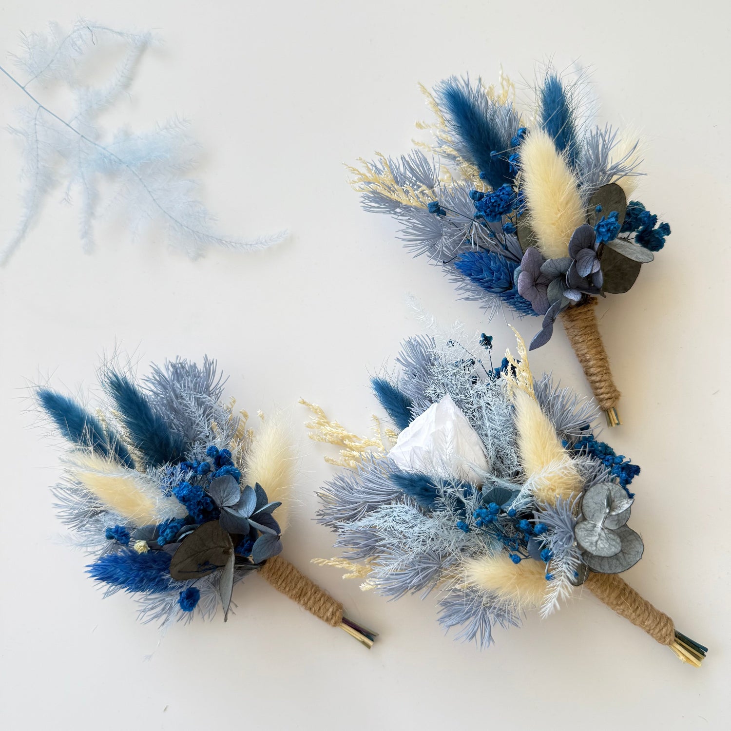 Set of three handmade blue and beige dried boutonnieres with natural jute stems, perfect for groomsmen gifts.