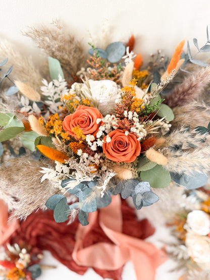 Bouquet of flowers with orange roses, greenery, and dried elements on a white background