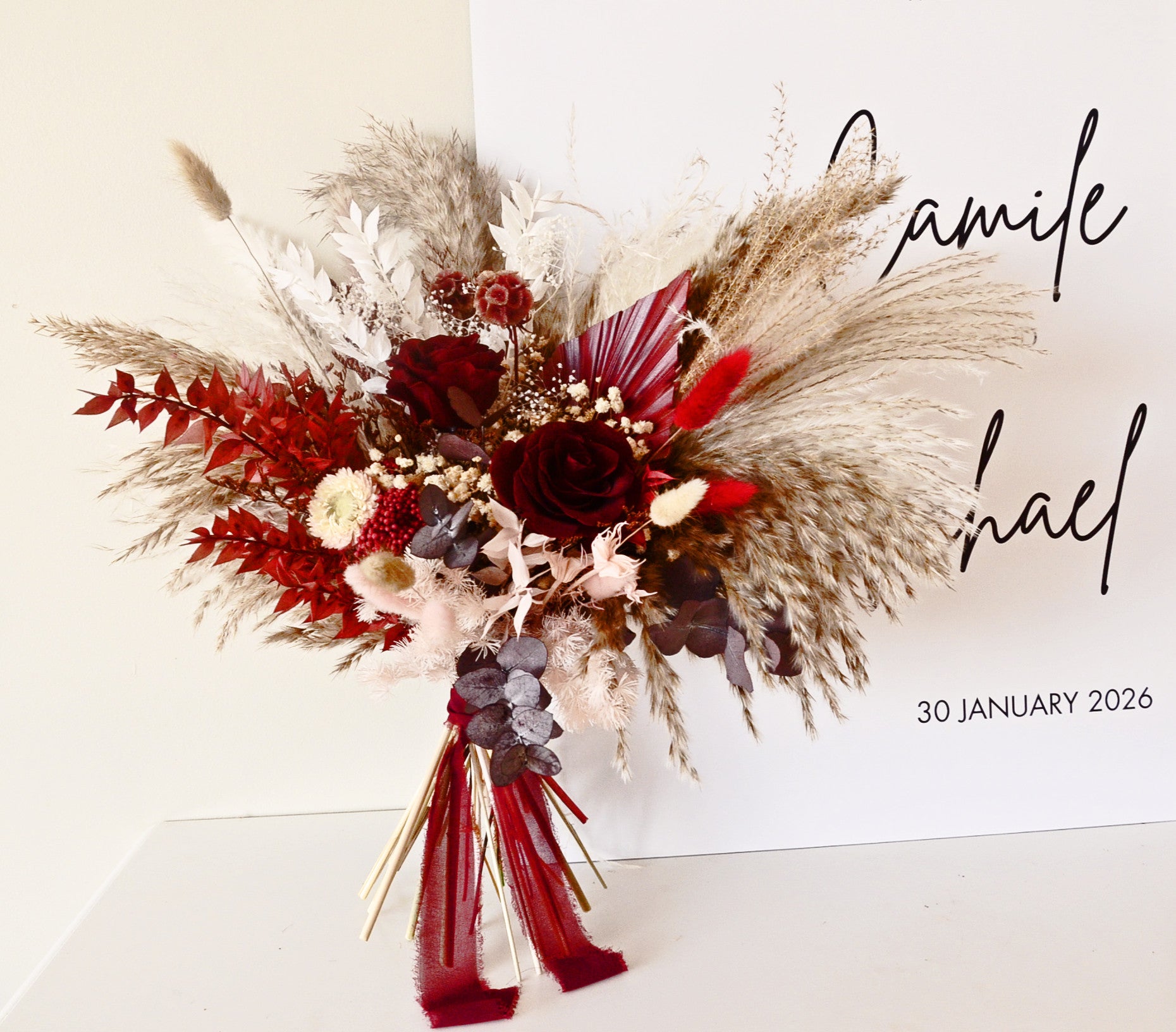 Dramatic dried bridal bouquet with burgundy roses, pampas grass, eucalyptus and rustic textures, boho wedding flowers.