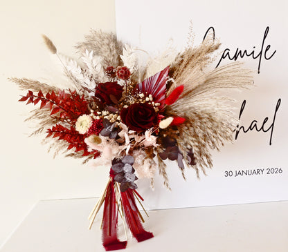 Dramatic dried bridal bouquet with burgundy roses, pampas grass, eucalyptus and rustic textures, boho wedding flowers.
