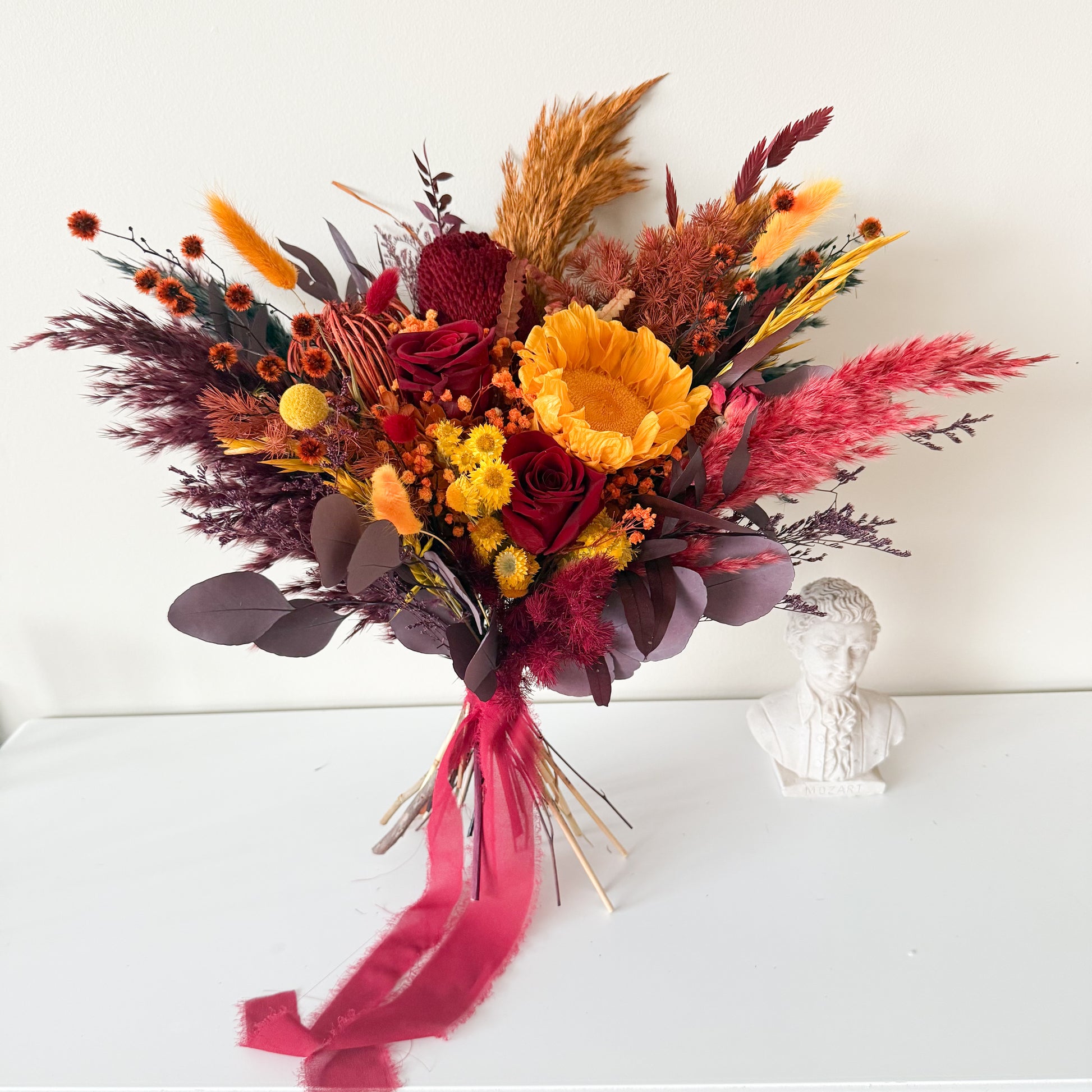 Dramatic dried bridal bouquet with burgundy roses, pampas grass, eucalyptus and rustic textures, boho wedding flowers.