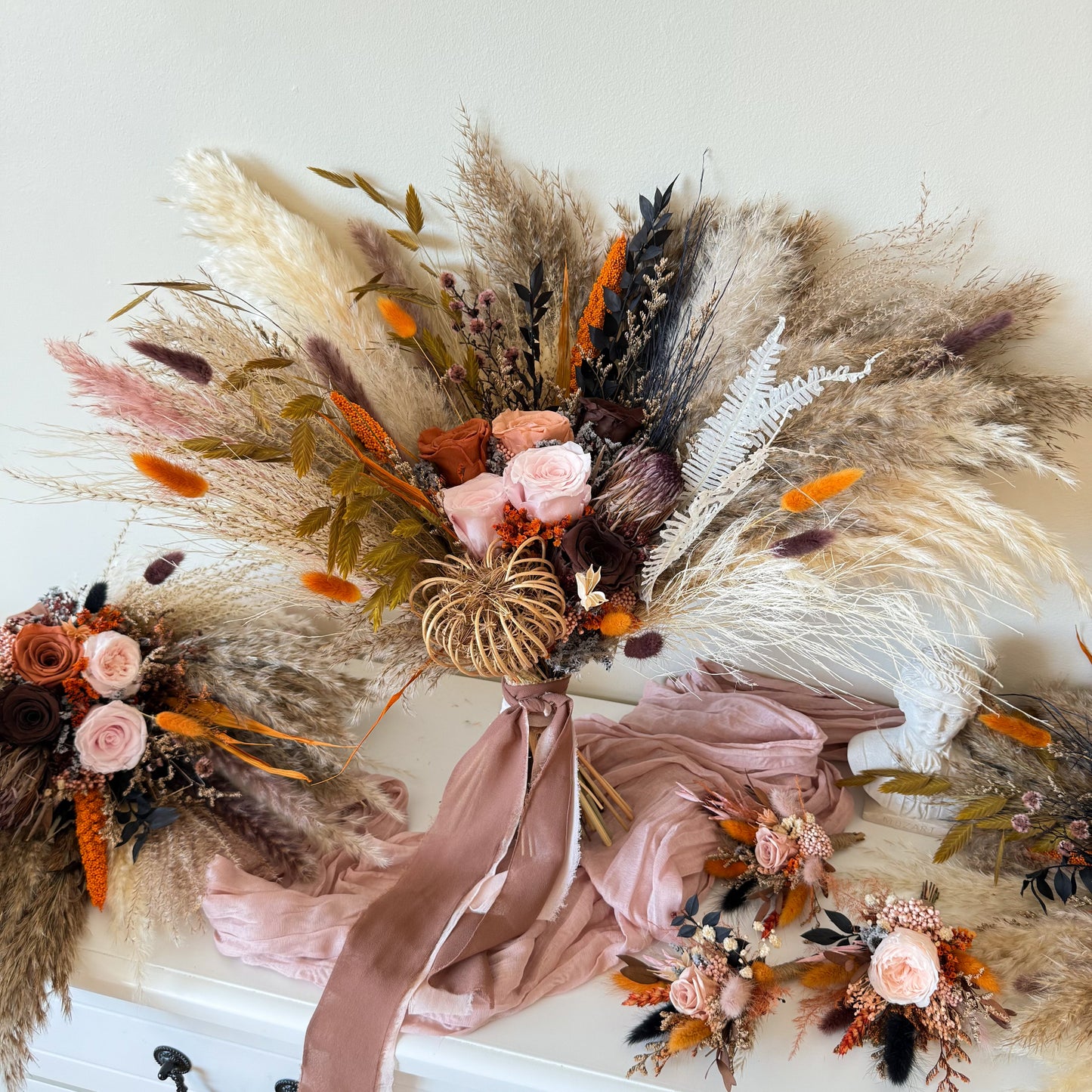Large boho bridal bouquet with pampas grass, preserved roses and matching wedding accessories in neutral terracotta tones.