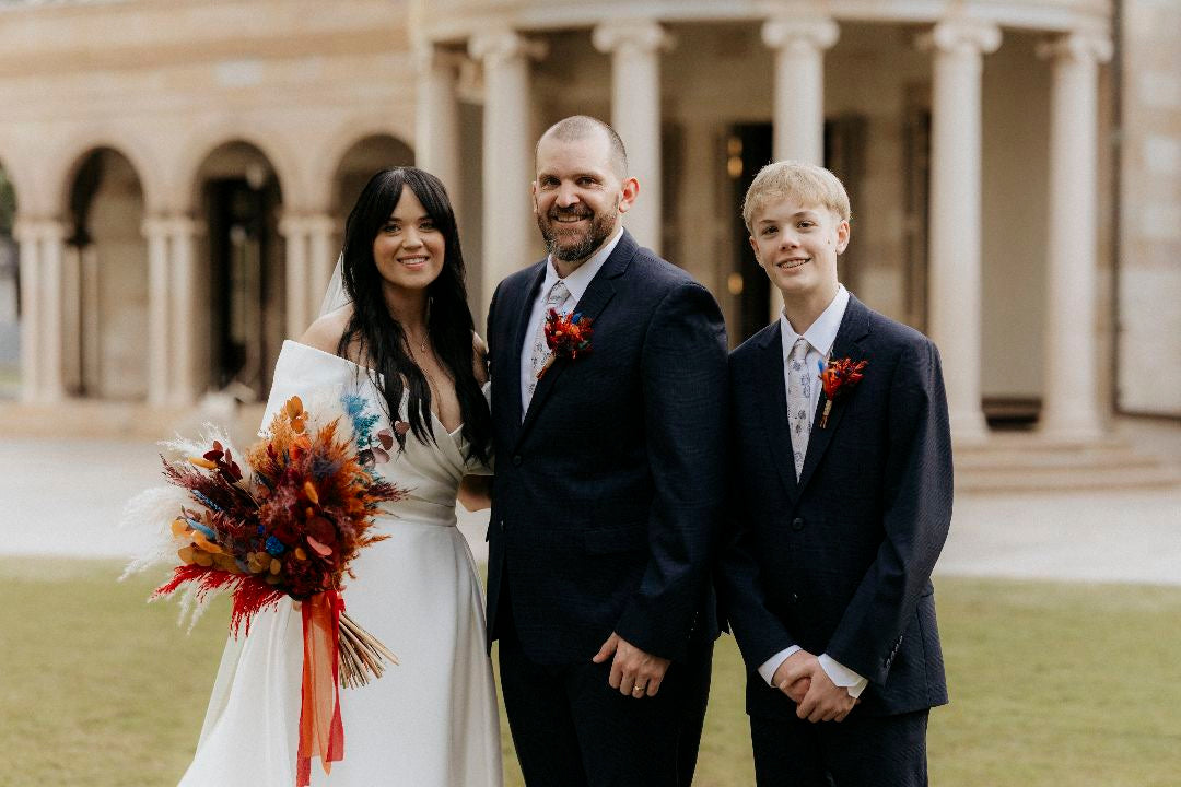 The bride holds a large autumn-themed dried bouquet with red, orange, and brown leaves.