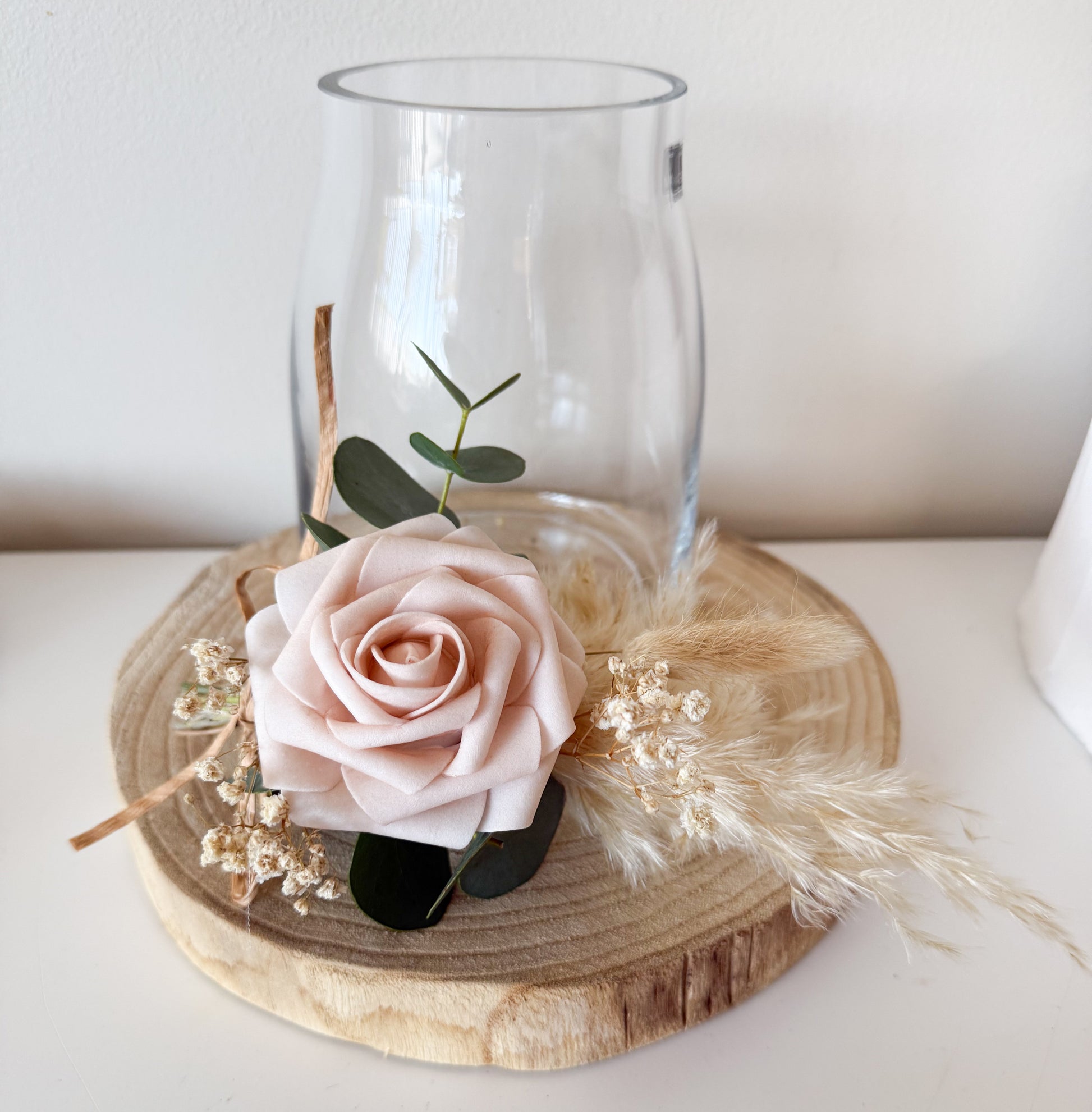 Boho table decor. Clear glass vase with a pink rose and greenery on a wooden coaster.
