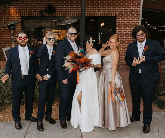  a bride in a white wedding gown holding a large autumn-colored feather bouquet, flanked by two groomsmen in navy suits and two boys in dark suits.