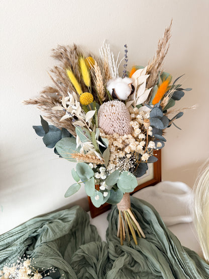 Bouquet of dried flowers with greenery and colorful accents on a white surface.