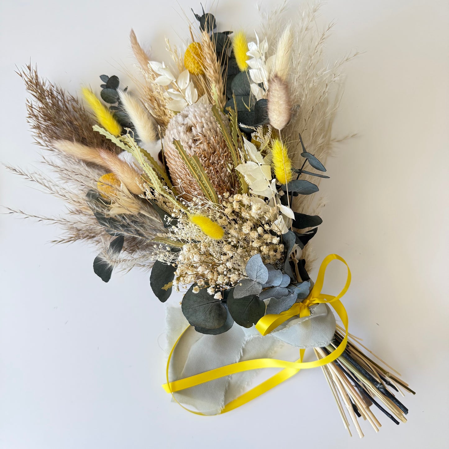 Bridesmaid dried flower bouquet in yellow and neutral tones featuring preserved eucalyptus, bunny tails, banksia and textured dried florals. Boho-style wedding bouquet with natural stems and yellow ribbon, perfect for rustic and modern weddings.