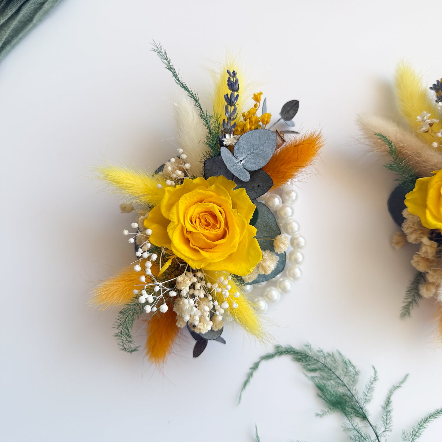 Bright yellow and orange preserved flower corsages on mannequin hands â€” dried floral accessories for wedding party.
