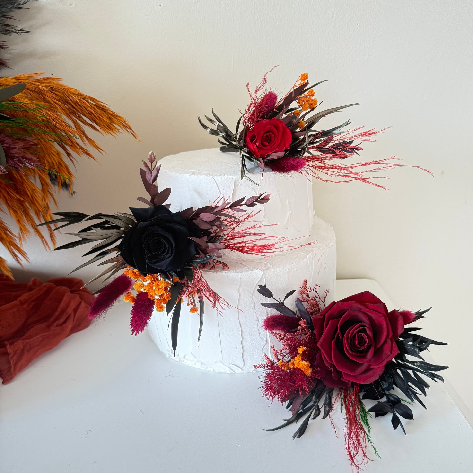 Burgundy and black preserved rose floral cake topper set on white tiered wedding cake
