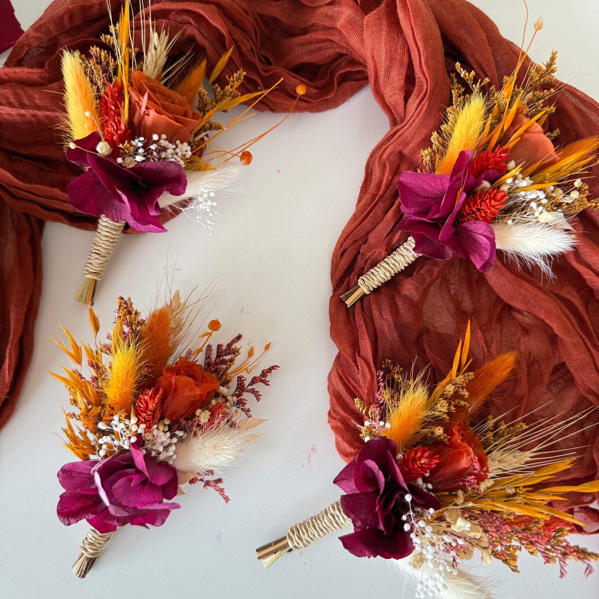 Autumn wedding boutonnieres featuring burgundy flowers, dried grasses and burnt orange accents