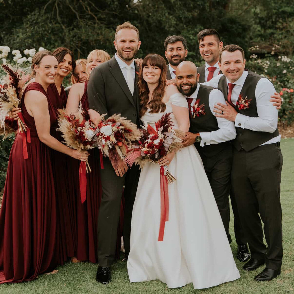 Bride and bridesmaids holding burgundy, red and ivory dried and preserved wedding flower bouquets with pampas grass at an outdoor wedding in Aust