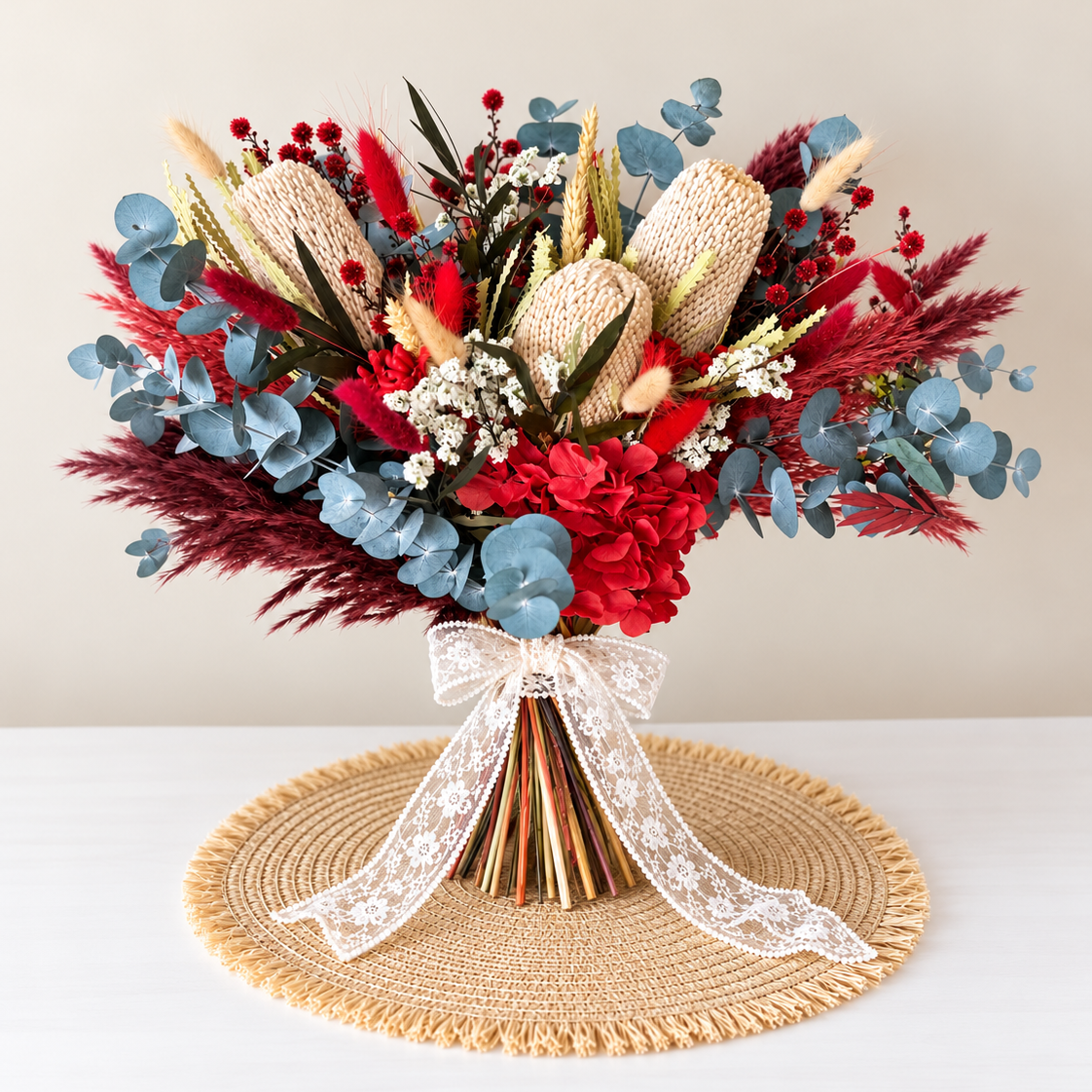 A statement dried and preserved bridal bouquet featuring rich burgundy and red tones, natural banksia, soft blue eucalyptus and delicate ivory lace ribbon. Perfect for rustic, boho and Australian native-inspired weddings.