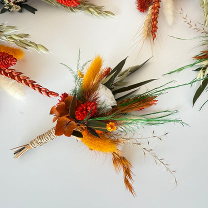 Set of dried boutonnieres in burnt orange with preserved roses, greenery and rustic accents for groom and groomsmen.