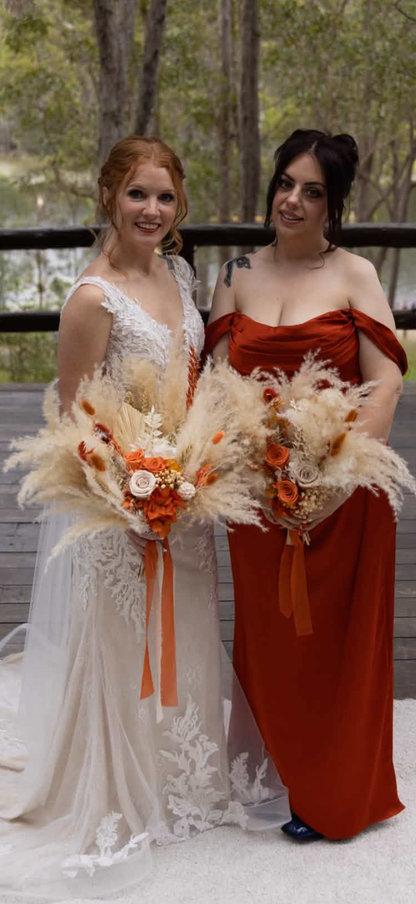Bride holding large pampas grass bouquets with orange and white flowers.