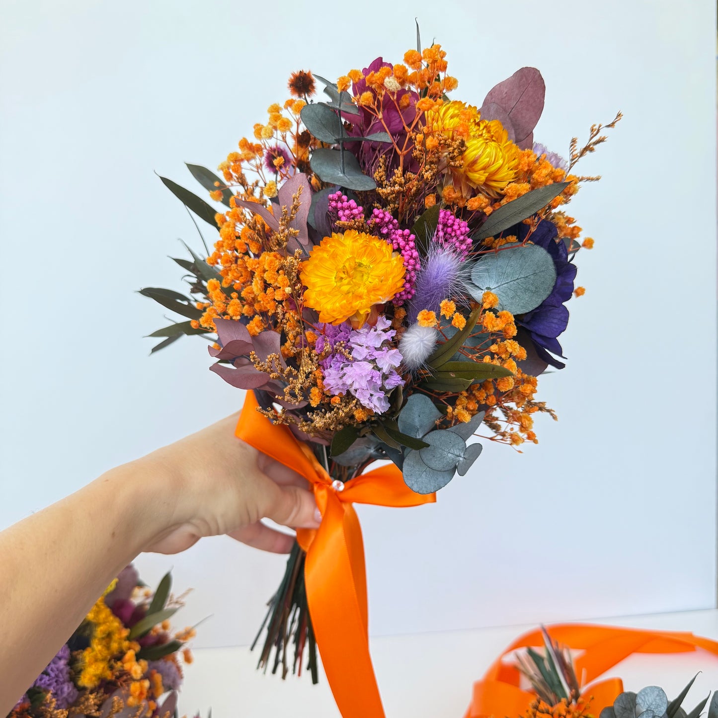 Bouquet of flowers with an orange ribbon held by a hand