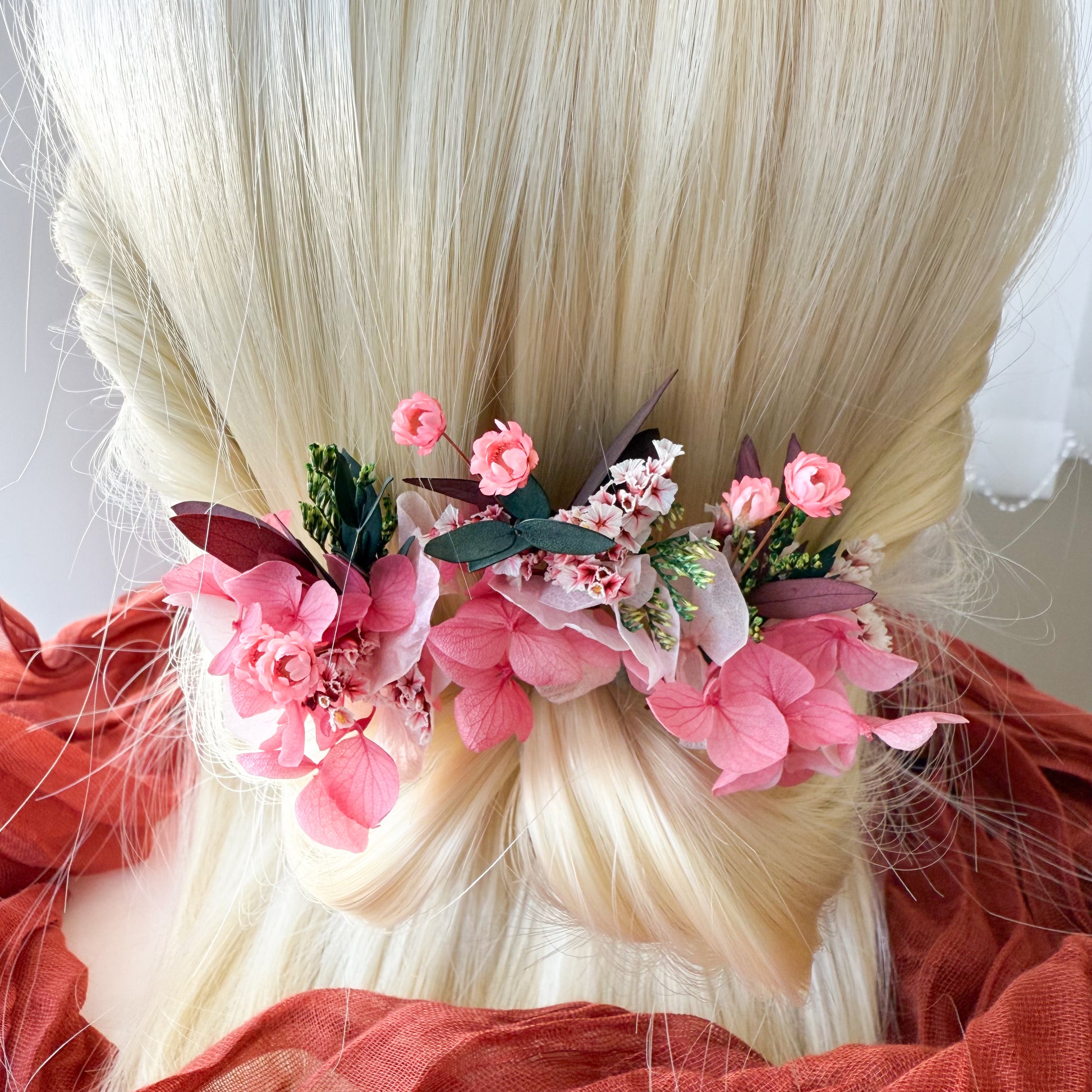  Bridal hair accessories featuring pink artificial blossoms and green foliage styled in a low twisted bun, perfect for brides or bridesmaids