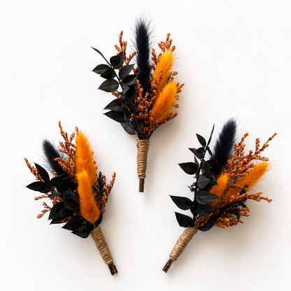 Three identical dried floral boutonniere-style arrangements on a plain white background. Each arrangement features bright orange fluffy grass, black leaves, a black feather, and small brown twig-like accents, with the stems wrapped in natural twine.