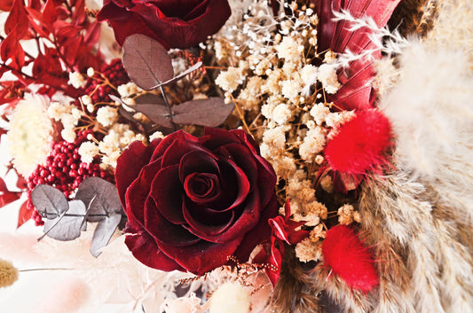 Close up of preserved burgundy rose with pampas grass, dried flowers and rustic textures for boho bridal bouquet.
