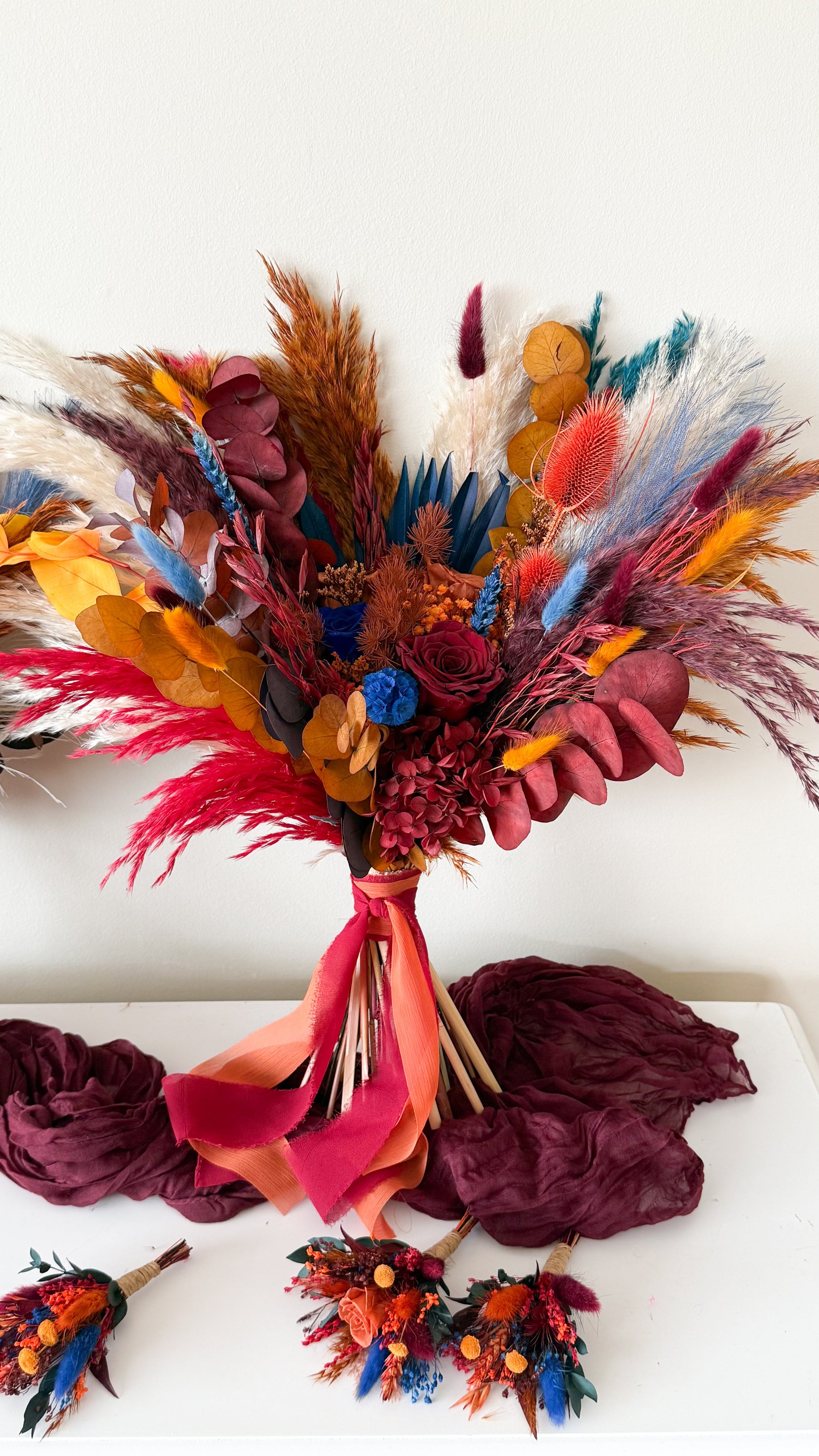 Colorful dried flower bouquet with red ribbon on a white surface