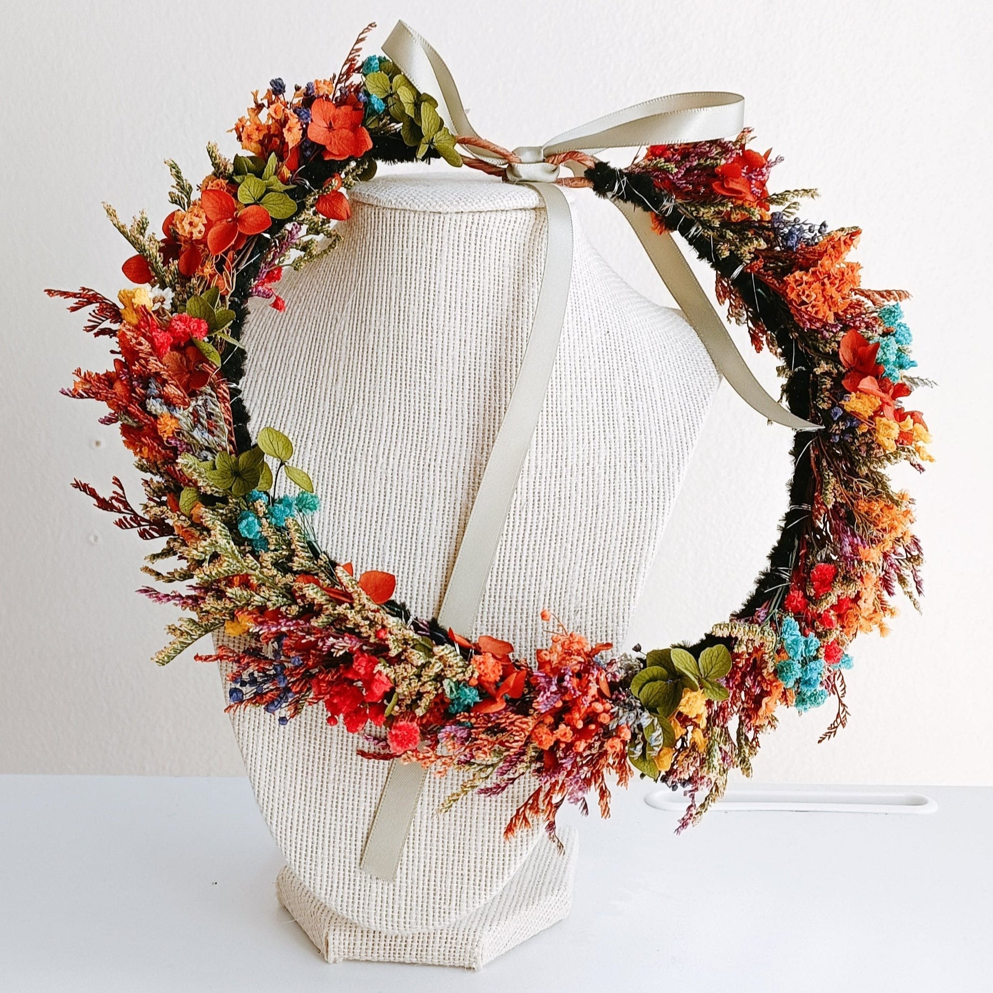 Colorful dried flower crown with red, orange, turquoise, and green accents, tied with a satin ribbon