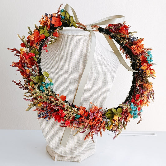 Colorful dried flower crown with red, orange, turquoise, and green accents, tied with a satin ribbon