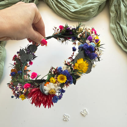 Hand holding a colorful flower wreath with green fabric in the background