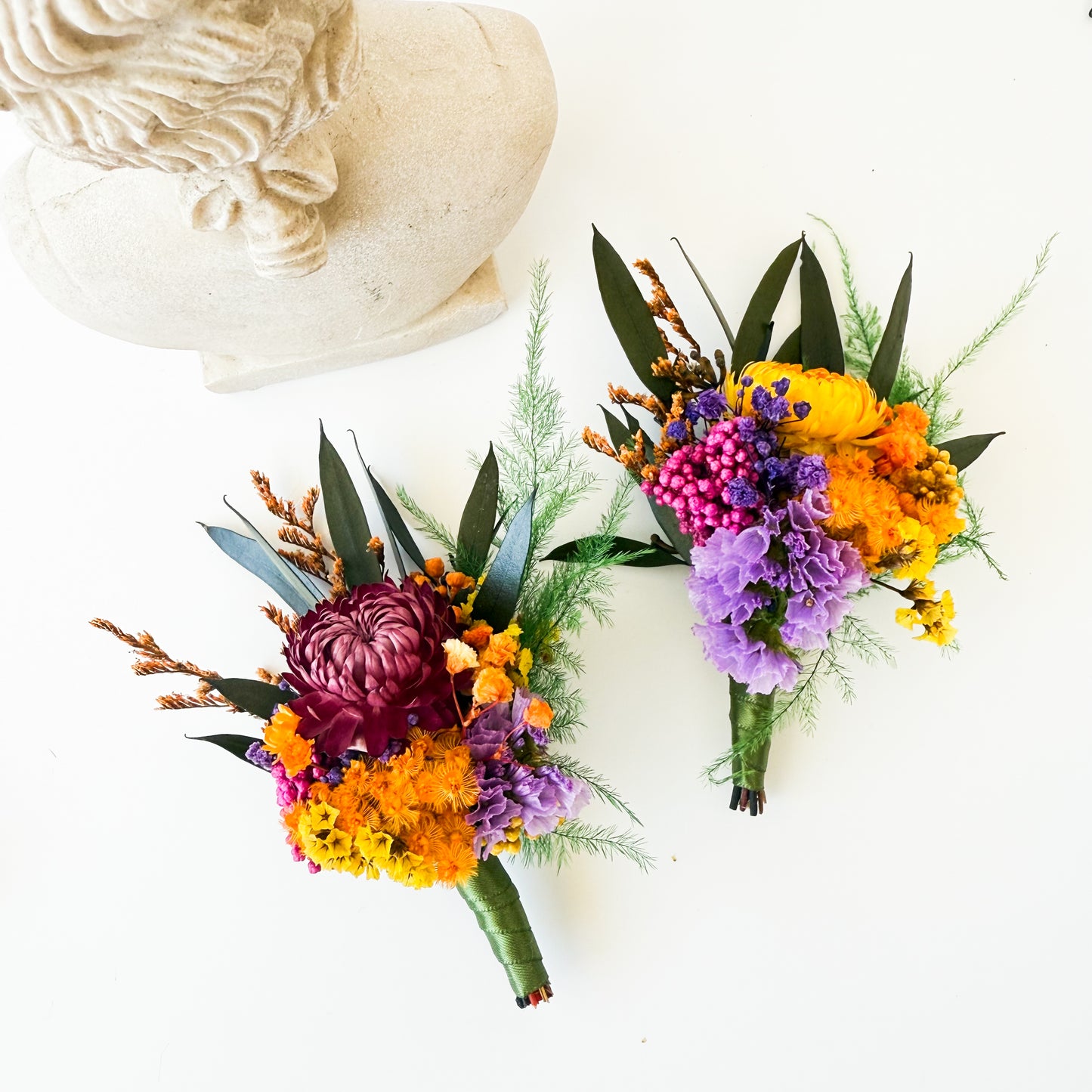 Two colorful flower bouquets on a white surface with a decorative stone object.