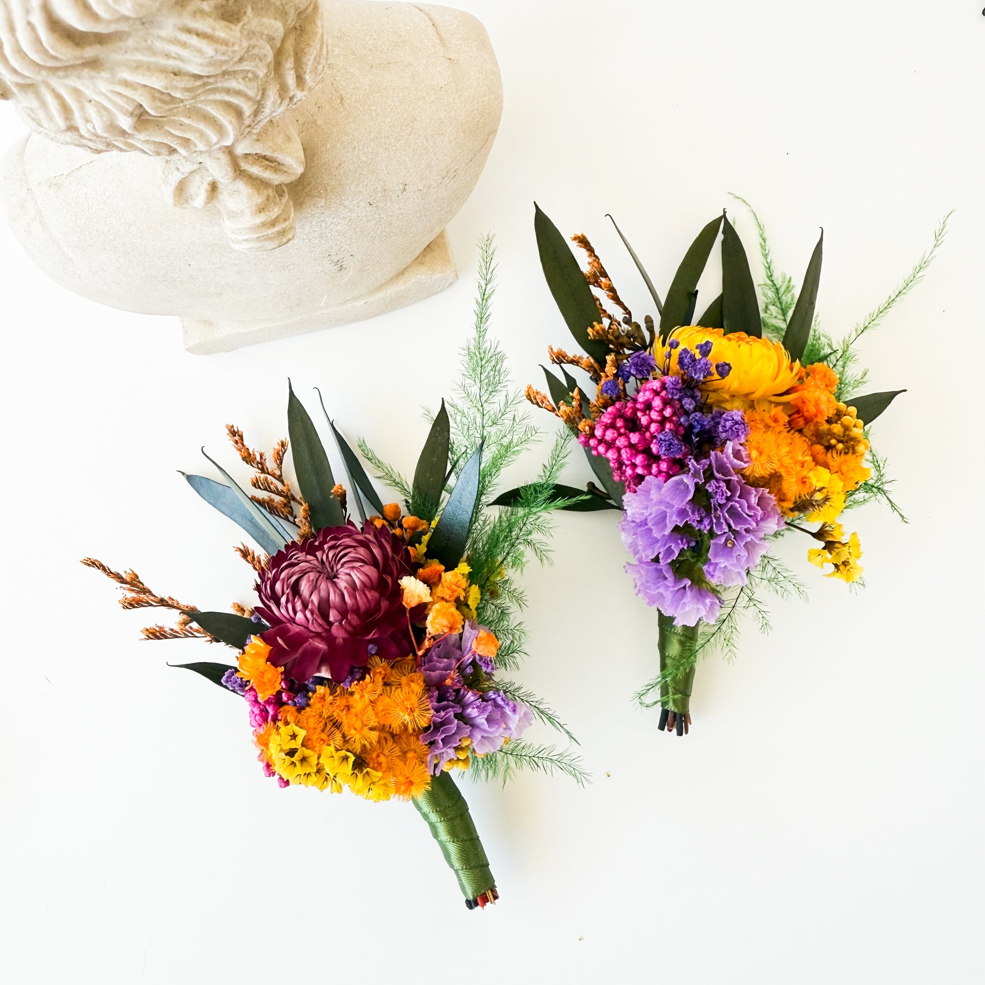 Two colorful flower bouquets on a white surface with a decorative stone object.