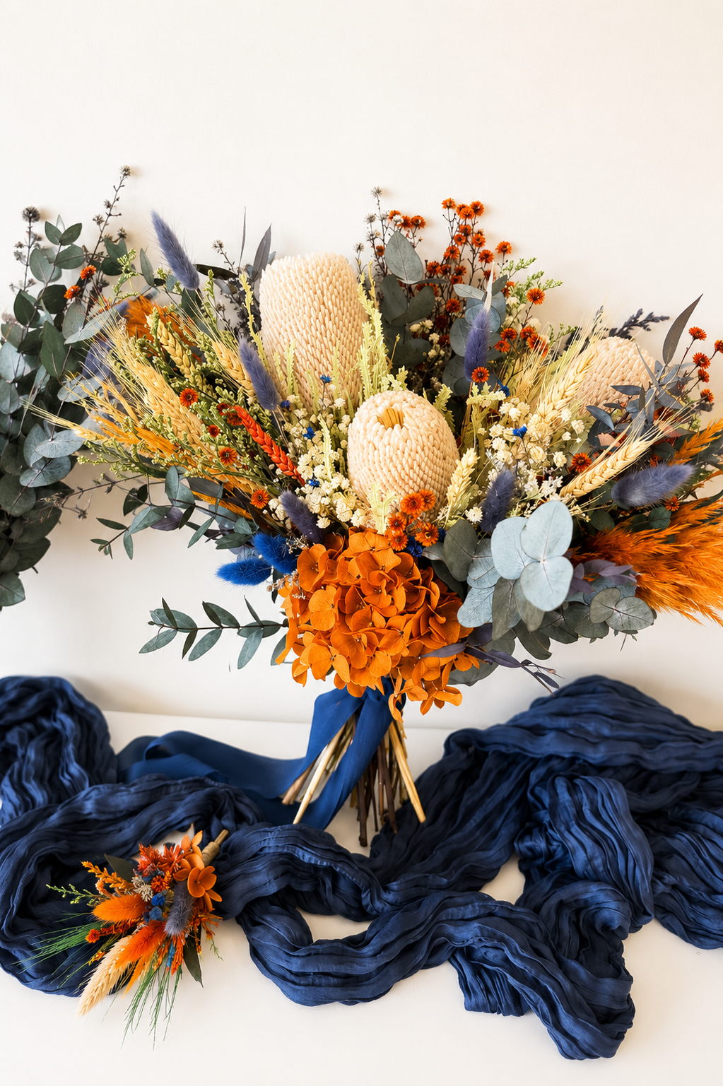 Complete Australian native wedding flower set including bridal bouquet, bridesmaid bouquet and matching dried wedding accessories in burnt orange and navy blue.