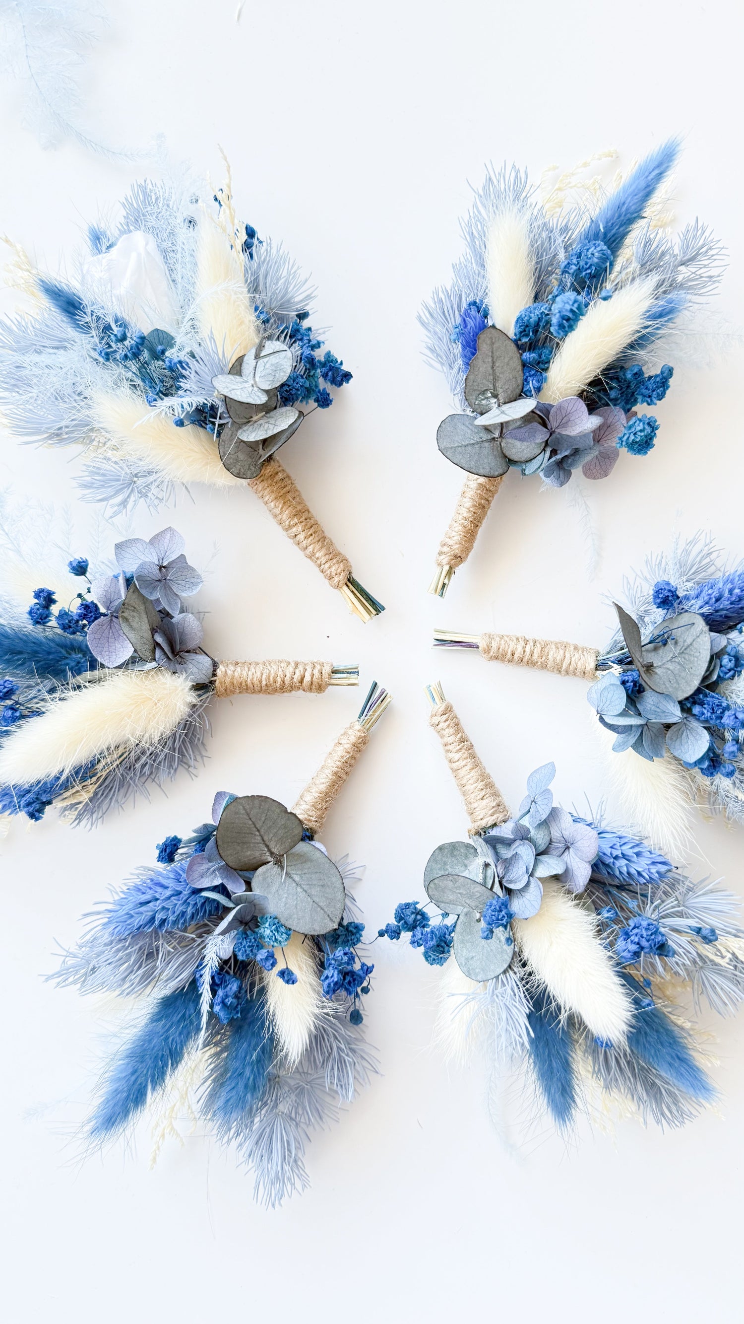 Collection of dried floral boutonnieres in dusty blue and ivory tones, preserved and handmade for elegant weddings.