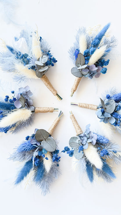 Collection of dried floral boutonnieres in dusty blue and ivory tones, preserved and handmade for elegant weddings.