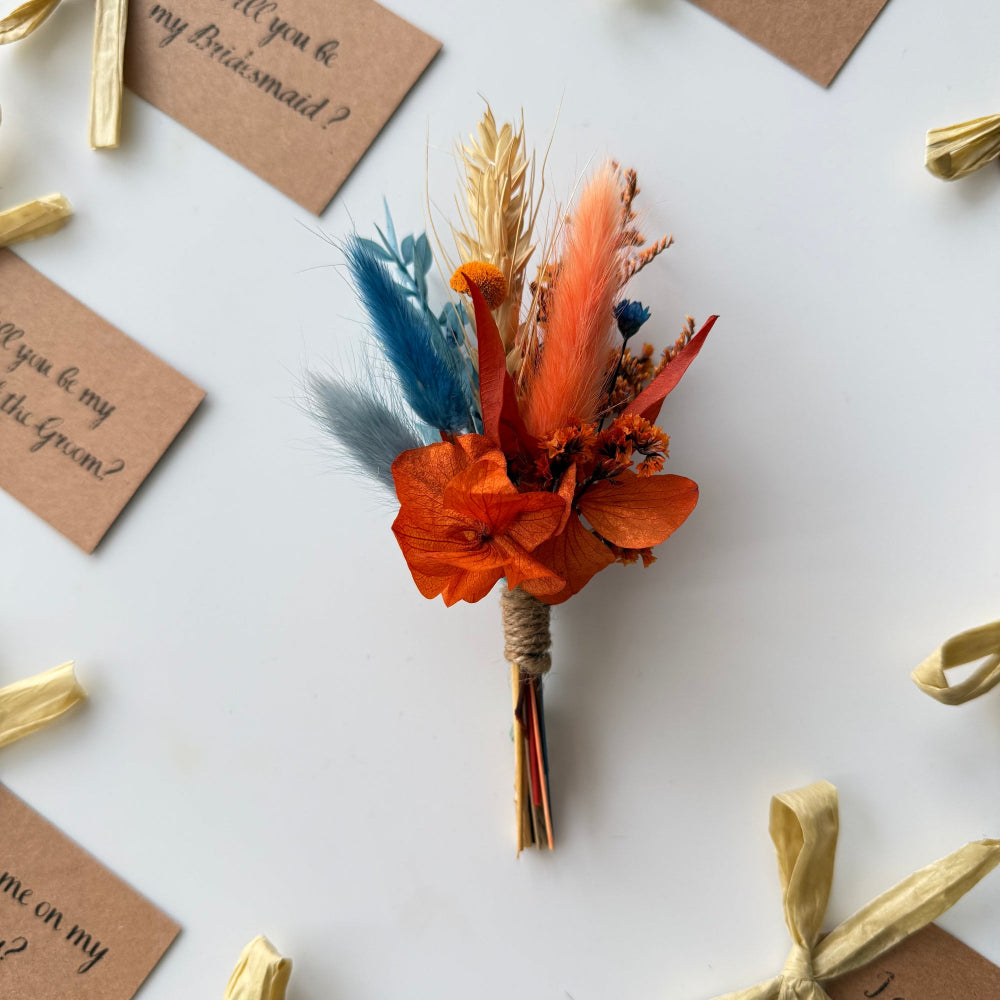 Dried flower bouquet with orange and blue flowers on a white surface with invitation cards.