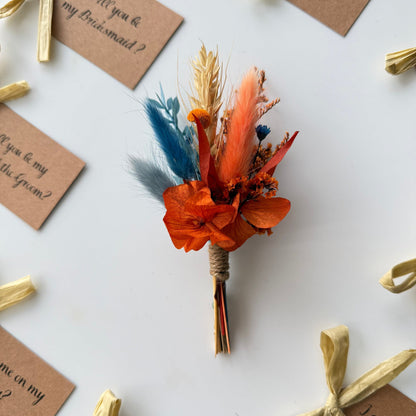 Dried flower bouquet with orange and blue flowers on a white surface with invitation cards.