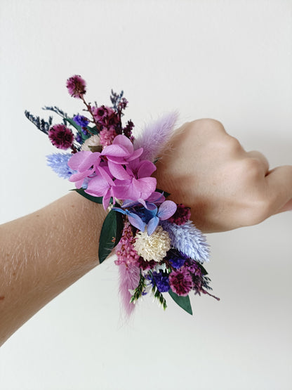 Dried flower wrist corsage in pink, burgundy, and lavender tones with preserved hydrangea and sola wood accents – perfect for bridesmaids or formal occasions.


