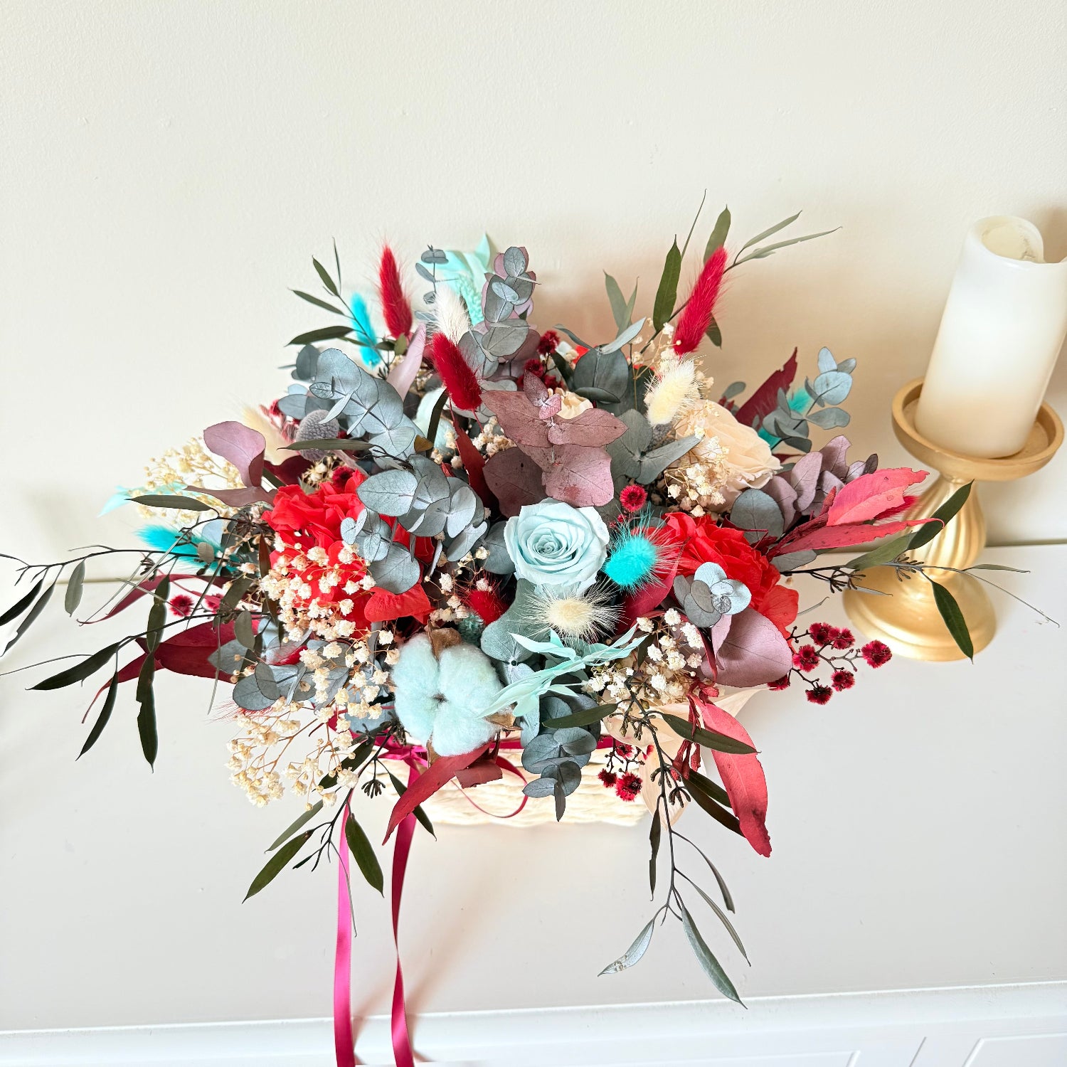 Festive dried flower Christmas arrangement in a wicker basket with preserved eucalyptus, cotton and red accents.