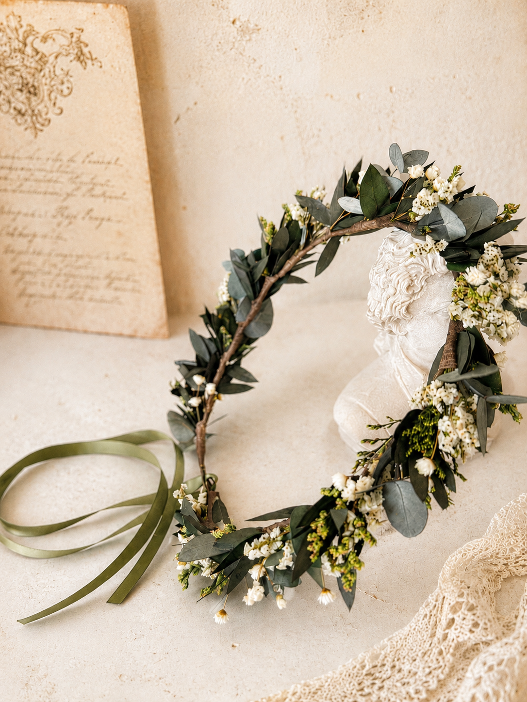 Green leafy wreath on a white surface with an antique book and lace fabric in the background