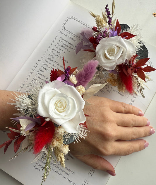 Floral wrist corsage with white roses and red feathers on a book page