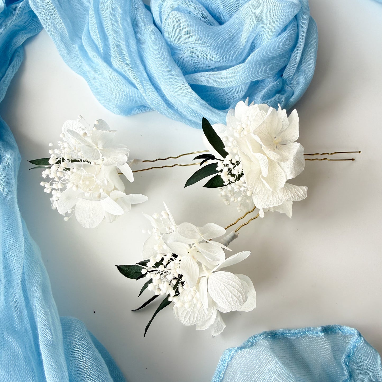 White floral hairpins with green leaves on a light blue fabric background