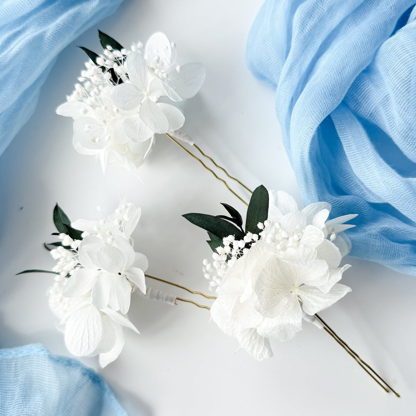 White floral hairpins with gold accents on a light blue fabric background