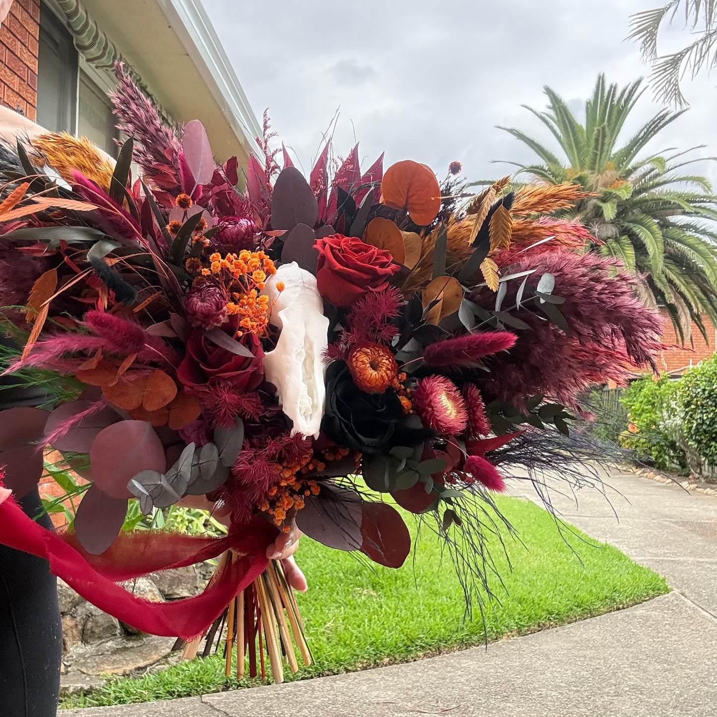 Colorful burgundy black bridal bouquet with red, purple, and orange flowers held by a person on a street.