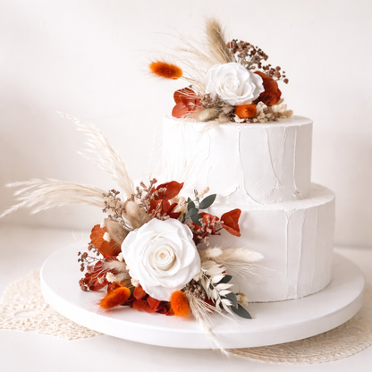 Two-tier white wedding cake decorated with ivory preserved rose and terracotta dried floral cake topper set in boho neutral style