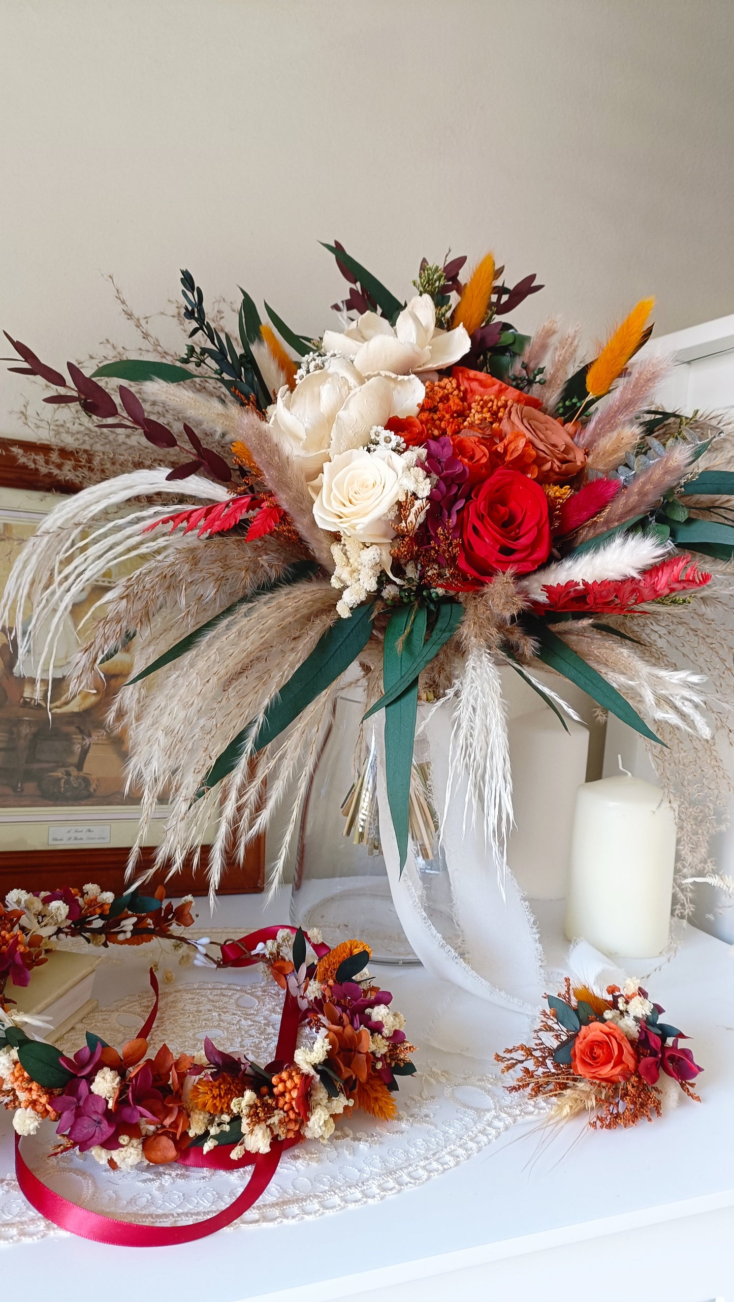Dried and preserved wedding bouquet with red roses and white flowers, styled with long pampas and eucalyptus stems, boho wreath in background