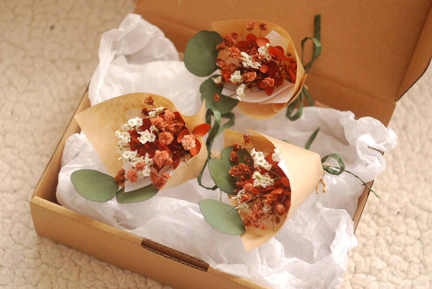 Mini bouquet in earthy terracotta and ivory tones, placed inside a kraft gift box lined with white tissue. Dried flowers include babyâ€™s breath, strawflowers, and eucalyptus. Ideal for wedding favours or small gifts. Presented in elegant eco-friendly packaging, perfect for rustic or boho-themed occasions.

