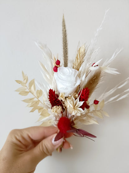 Mini bouquet or boutonnière with preserved red berries, bleached foliage, white sola roses and dried grasses. Wrapped with red ribbon, perfect as a groom's boutonnière or bridesmaid accessory for coordinated wedding sets.