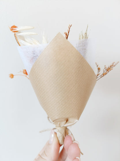 Minimalist view of a mini dried bouquet in kraft paper wrapping, shown from the back while being held in hand. Neutral background puts focus on the natural bouquet style. Features include preserved flowers and delicate wrapping â€” a great choice for wedding favours or eco-friendly small gifts. Suits rustic, terracotta, and country-style event themes.