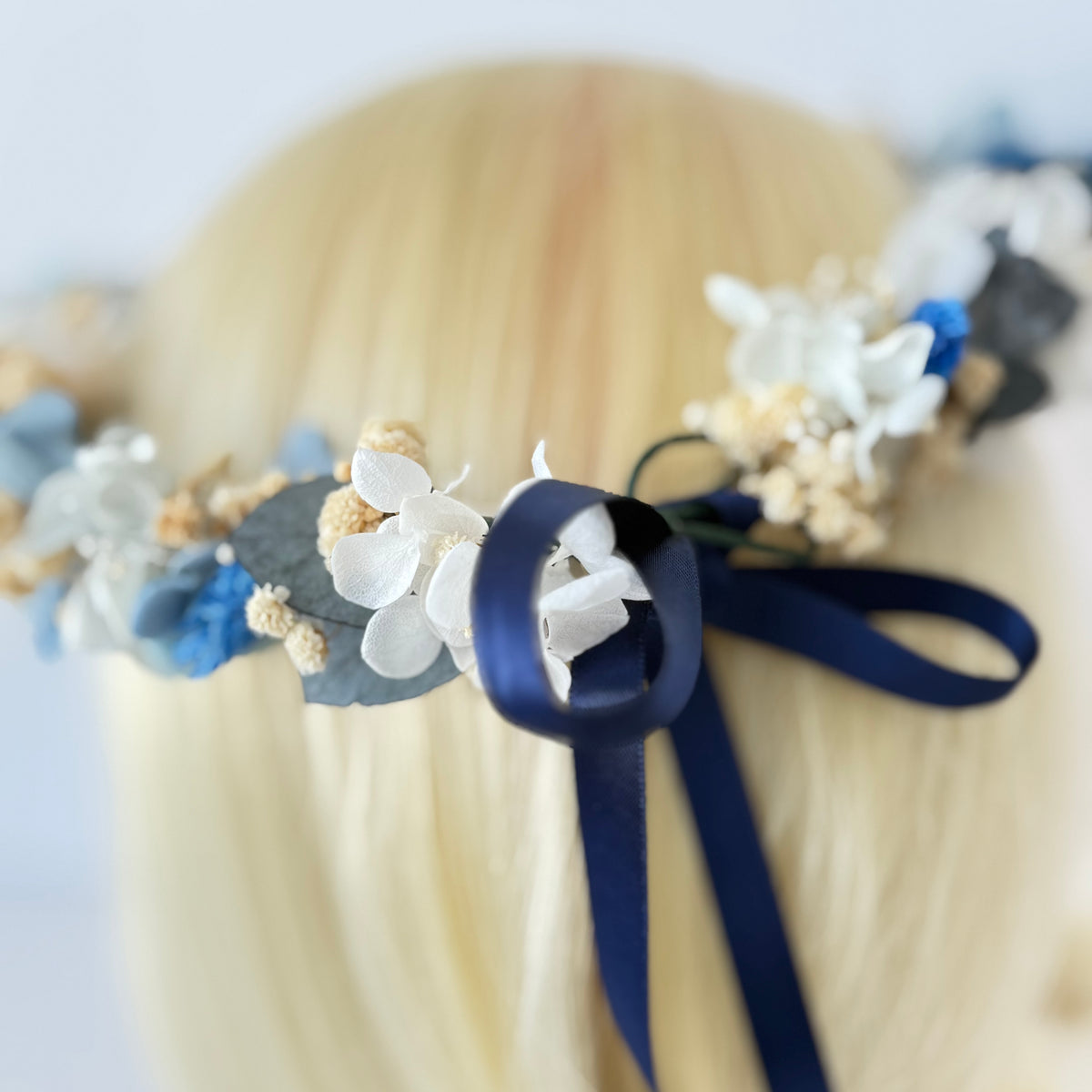 Floral headband with blue ribbons on a person with blonde hair.
