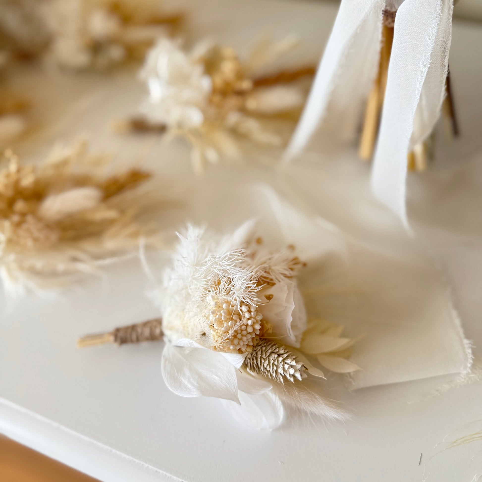 Decorative boutonniere with dried flowers and feathers on a white surface
