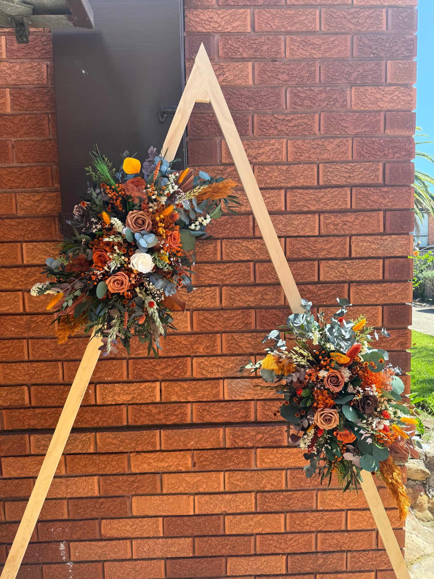 Boho wedding arbor decorated with large dried flower arrangements in burnt orange, rust and natural tones.