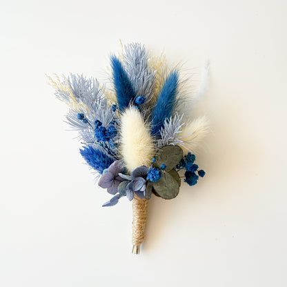 Rustic dried flower boutonniere with blue preserved blooms and ivory bunny tails, ideal for boho wedding theme.